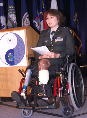 Foto: Asistente Del Secretario Duckworth, quien se sienta en una silla de ruedas junto a un podio, tiene dos piernas prostéticas. 