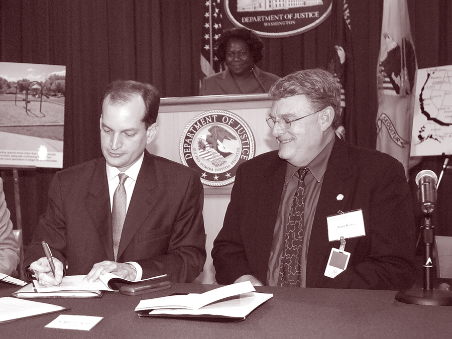 Photo of Former Assistant Attorney General R. Alexander Acosta signing PCA Agreement between DOJ and Taos County, New Mexico, at August 2004 DOJ ceremony with Deputy Assistant Attorney General Loretta King and James Dennis, Human Resources Director and ADA Coordinator for Taos County, New Mexico, looking on.