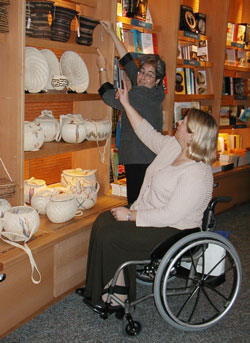 Photo: Museum shop interior where woman using wheelchair points out item for staff to retrieve.