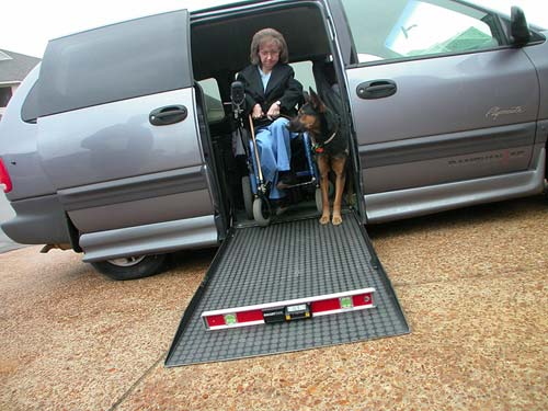 woman using a wheelchair rolls down ramp from van