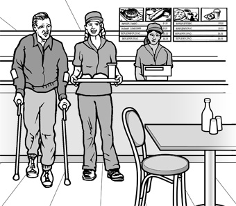 In a casual restaurant, an employee assists a man using crutches, by carrying his tray to a table.
